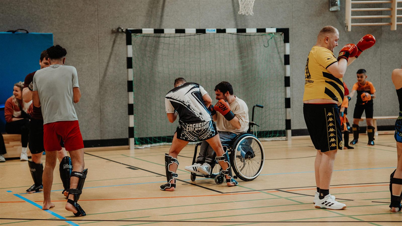 Inklusives Kampfsport-Training – ein Athlet im Rollstuhl trainiert Muay Thai mit Pratzen, umgeben von Mitstreitern